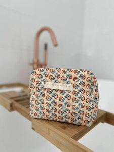 Toilettas met blokprint in de kleuren creme wit en koraal van het merk La p'tite Cachottière. De toilettas staat op een rekje van bamboe bij het bad met een koperkleurige kraan.