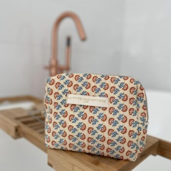 Toilettas met blokprint in de kleuren creme wit en koraal van het merk La p'tite Cachottière. De toilettas staat op een rekje van bamboe bij het bad met een koperkleurige kraan.