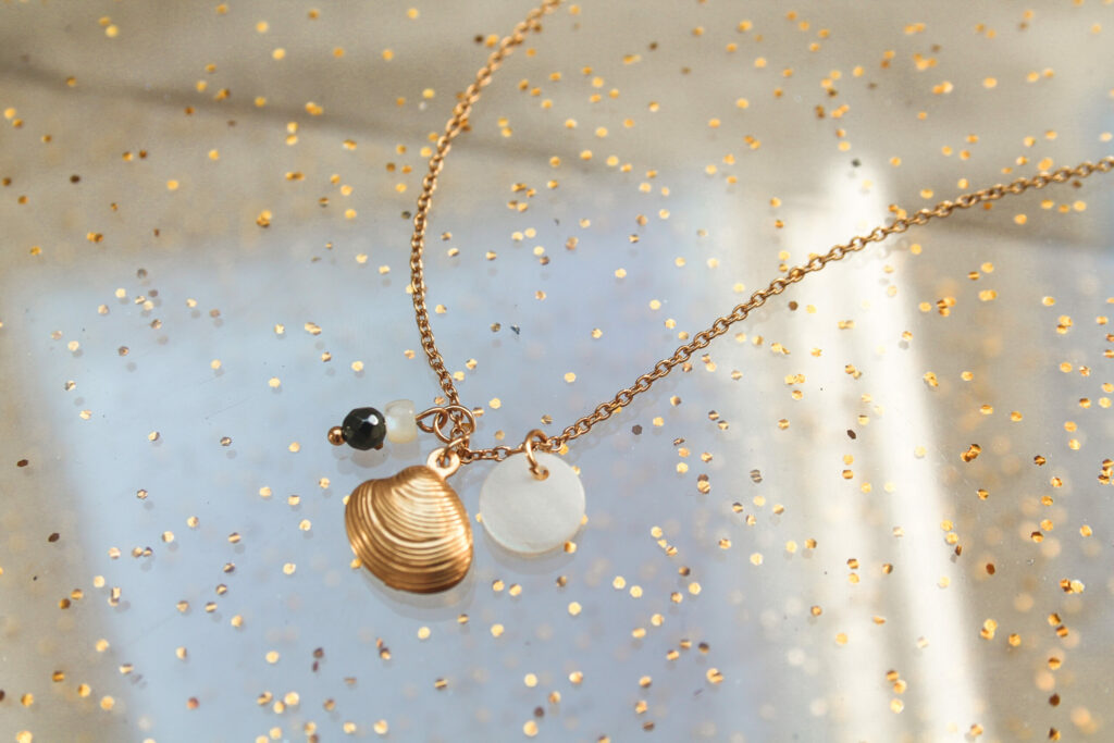 Goudkleurige ketting van stainless steel met Hematiet, een muntvormige schelp en een extra bedeltje in de vorm van een schelp. De ketting is 50 cm lang
