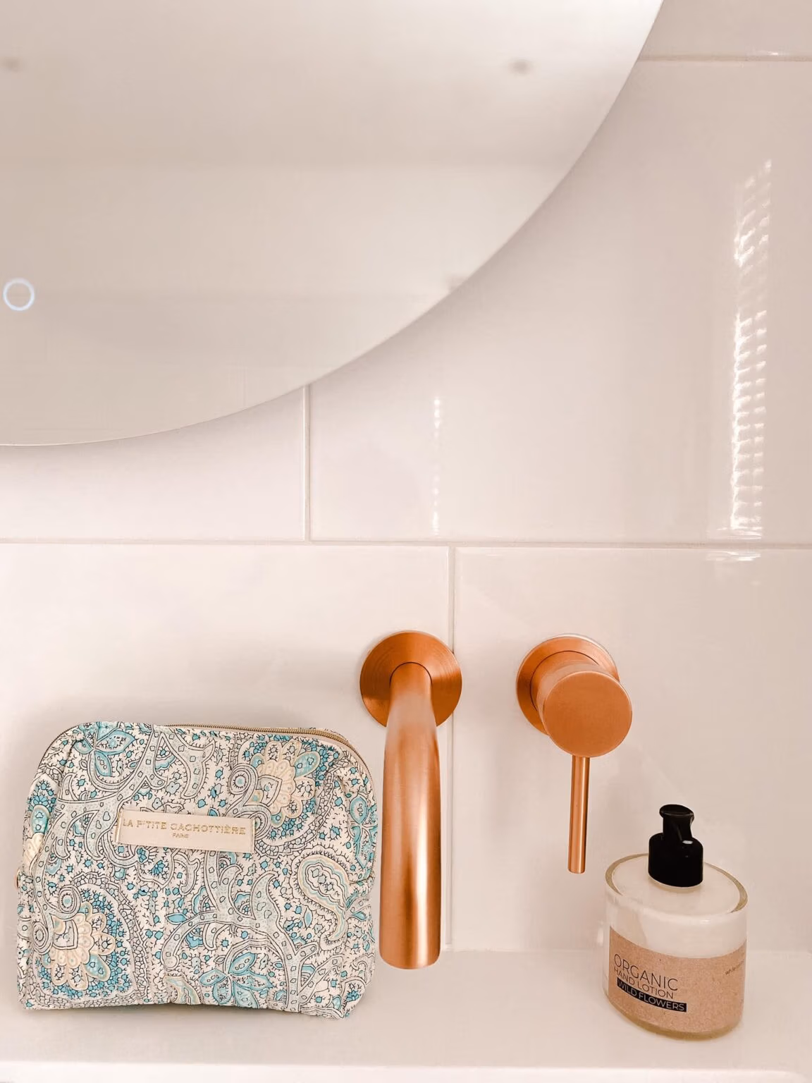 Make-up tas Blue met blokprint in de kleuren crème wit en turquoise van het merk La p'tite Cachottière. De make-up tas staat op een wastafel met een koperkleurige kraan en spiegel met een handlotion ernaast.