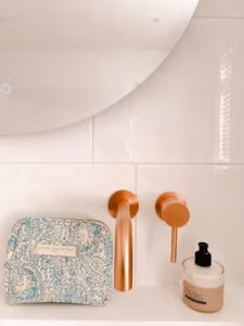 Make-up tas Blue met blokprint in de kleuren crème wit en turquoise van het merk La p'tite Cachottière. De make-up tas staat op een wastafel met een koperkleurige kraan en spiegel met een handlotion ernaast.