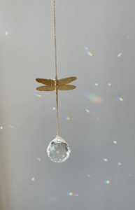 Raamkristal met een goudkleurige libelle hanger, hangend in een venster en reflecterend natuurlijk licht met een kleurrijk regenboog effect.