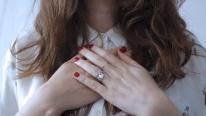 vrouw met haar handen op haar borst bij haar hart met rode nagels en bruin haar. En een zilveren ring met een hartje.