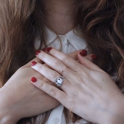 vrouw met haar handen op haar borst bij haar hart met rode nagels en bruin haar. En een zilveren ring met een hartje.