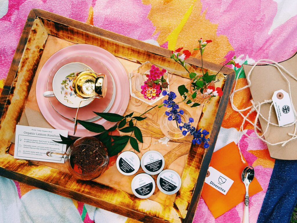 Gekleurd picknick kleed met daarop een houtendienblad met daarop een roze kop voor kruidenthee en een theezeefje. Daarnaast staan er nog wat kleine vaasjes me bloemen.