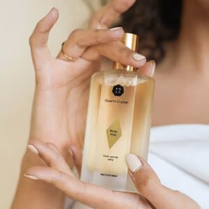 Vrouw houd de Anas body mist vast ze draagt een witte omslagdoek en heeft donker haar.