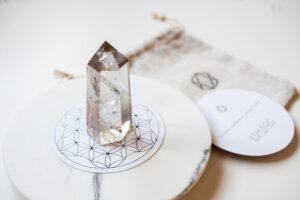 Bergkristal op een witte ronde ondergrond met een zandkleurige stoffen cadeauzakje en een wit rond kaartje.