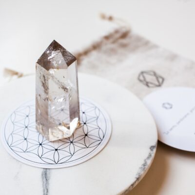 Bergkristal op een witte ronde ondergrond met een zandkleurige stoffen cadeauzakje en een wit rond kaartje.