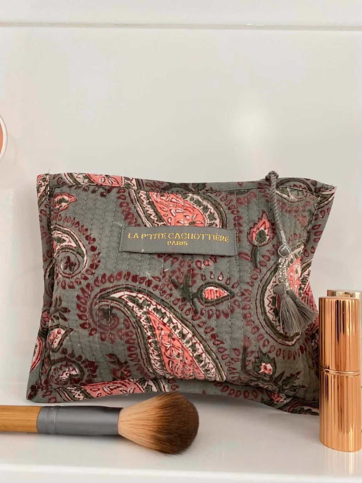 Make-up tas grijs blokprint in de kleuren grijs, roze, crème wit van het merk La p'tite Cachottière. De toilettas staat op een wastafel er staan wat make-up artikelen naast.