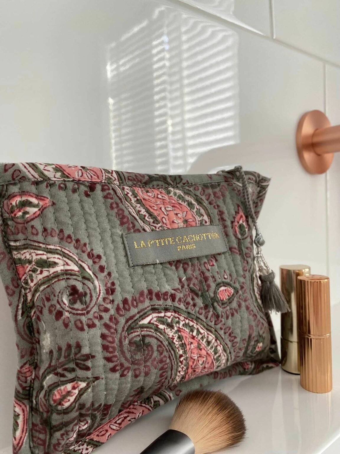 Make-up tas grijs blokprint in de kleuren grijs, roze, crème wit van het merk La p'tite Cachottière. De toilettas staat op een wastafel er staan wat make-up artikelen naast.