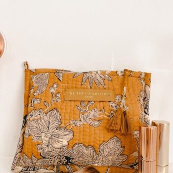 Make-up tas India met blokprint in de kleuren okergeel crème wit en blauw van het merk La p'tite Cachottière. De toilettas staat op een wastafel er staan wat make-up artikelen naast.