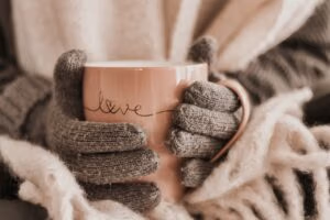 Vrouw met warme handschoenen houdt een beker vast met de tekst 'Love', terwijl de afbeelding verwijst naar het thema: 'Winterdip? Deze tips helpen.