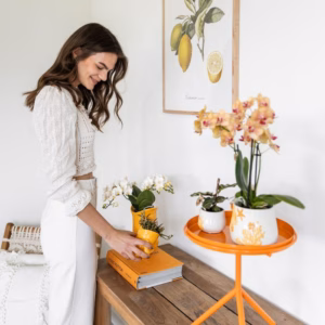 Vrouw in stijlvol interieur met de Gele Vis Vaas Plantenpot en andere keramische potten en vazen gevuld met bloemen en planten.
