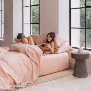 Vrouw die ontspannen op het Coco & Cici Tencel beddengoed perzik ligt in een lichte, moderne slaapkamer.
