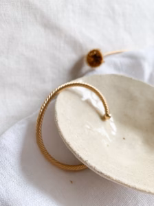 Goud vergulde open armband met gedraaid design op keramisch schaaltje