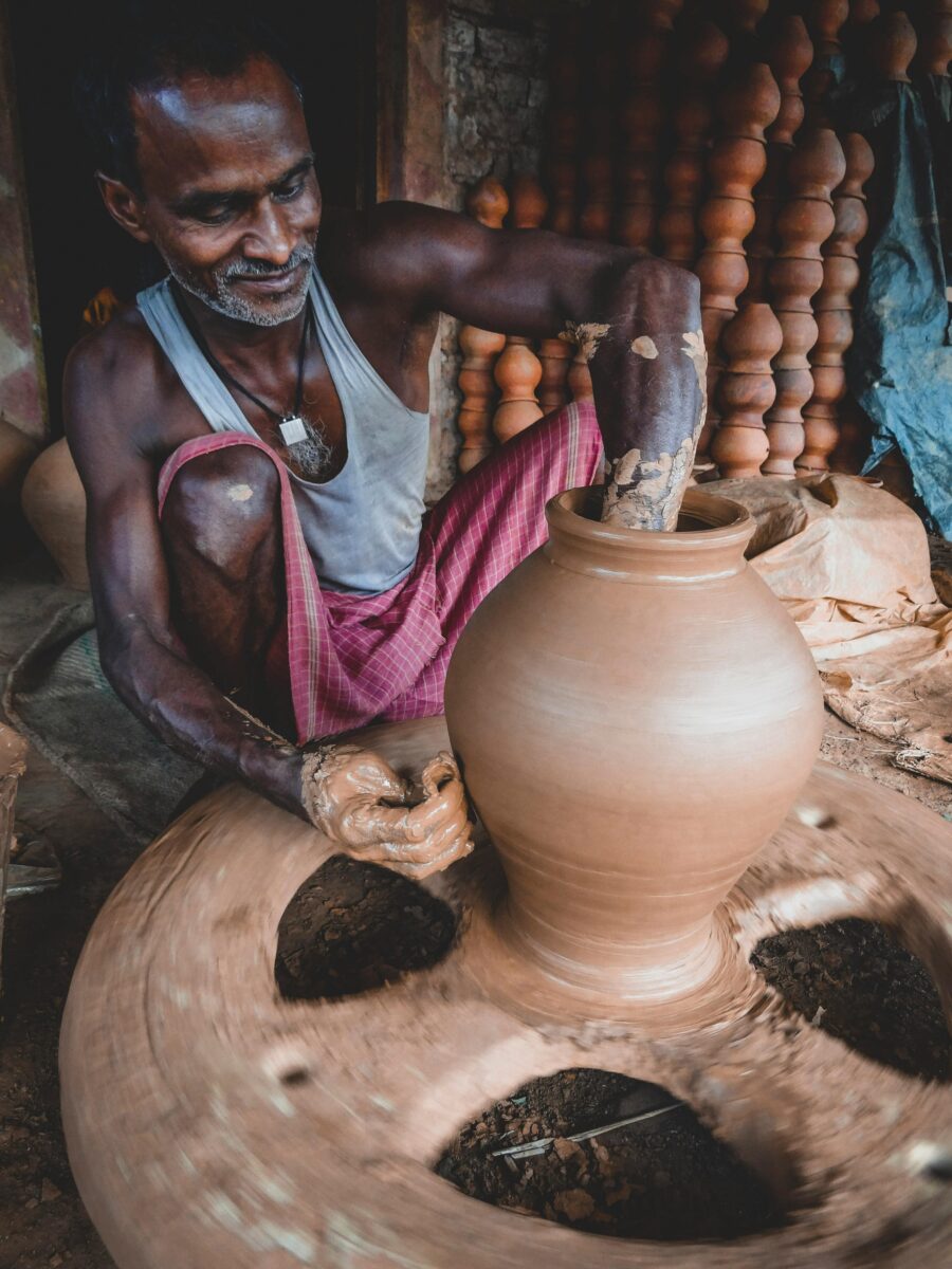A man expertly crafts a clay vase on a traditional pottery wheel in a rustic setting.